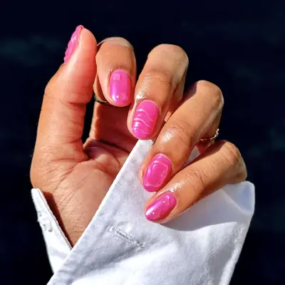 Hand displaying shiny, manicured nails with a wavy design, sleeves visible at the wrist