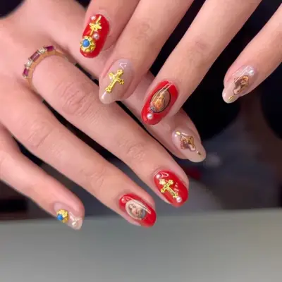 hand modeling baroque manicure with some red nails and some nude nails, with decals like gold crosses, biblical saints, and gems