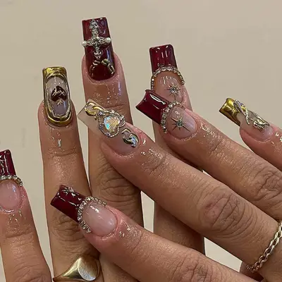 hand modeling nails with bare base and red tips with tons of silver rhinestones, with other nails featuring full red nails with gold accents, and other nails with bare bases and gold accents