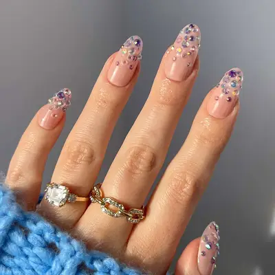 a neutral manicure topped with multicolored gemstones in shades of purple