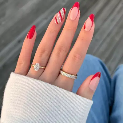 close up of hand showing off christmas manicure, with each nail different some plain red, some red french tips, and one with candy cane stripes