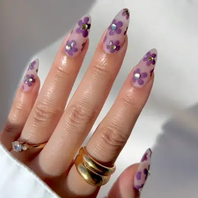 Manicure with translucent base and purple daisy designs with gems