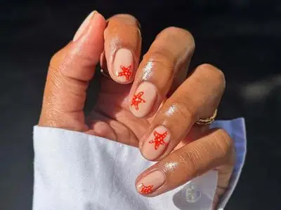 Hand with red starfish nail art on light nail polish and white shirt sleeve visible