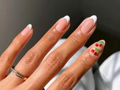 Hand with manicured nails, one nail featuring a design with small cherries