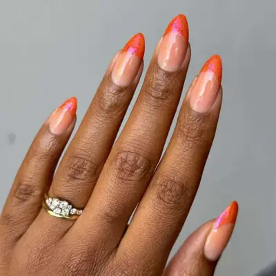 Manicured hand with orange nail polish, wearing gold rings with diamonds