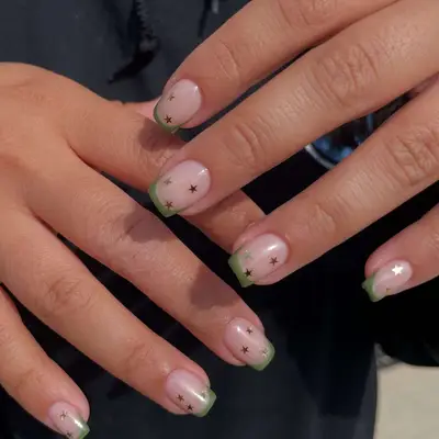 Close-up of human hands with nail art featuring green tips and small star accents