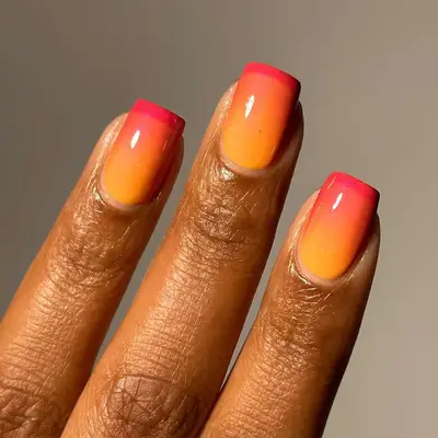 a hand with an orange and red sunset french manicure