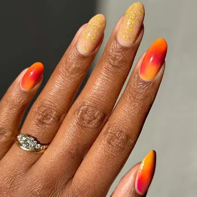 a hand with red and orange sunset and gold flecks manicure