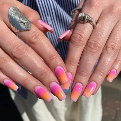 two hands with a pink and orange sunset manicure