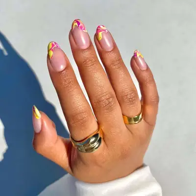 A hand displaying manicured nails with intricate yellow and pink designs; rings adorn the fingers
