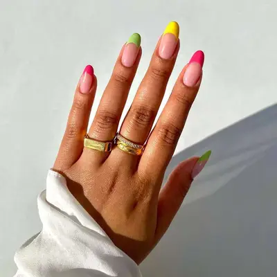 A hand with colorful manicured nails and rings on the fingers, sleeve visible