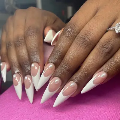 Close-up of manicured hands with pointed nails featuring a pink and white French design, a ring on one finger