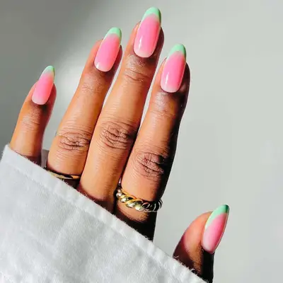 Hand with manicured nails in pink and green shades, wearing gold rings