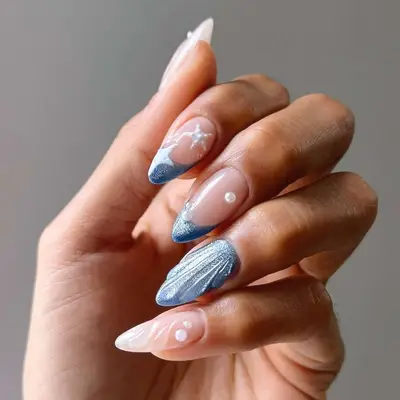 Manicured hand with blue and white nail art featuring intricate designs