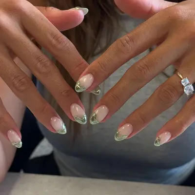 Hands with green French-tipped nails and a ring on the left ring finger