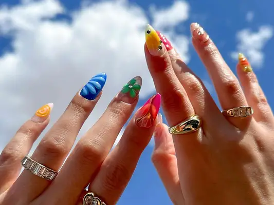 Mismatched manicure on hands held toward the blue sky