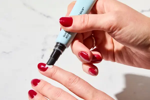 A person applying Butter London QuickFix Moisturizing Cuticle Balm to their nail beds