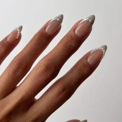 Close-up of manicure with white chrome French tips, pearls, and bow designs