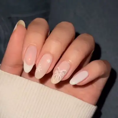 Manicure with neutral base, sparkly bow design, French tip, and snowflake designs