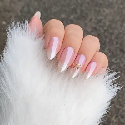 Hand with long almond nails with a baby pink polish, bow-shaped nail gemstone and chrome finish.
