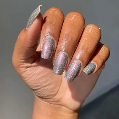 Hand with long square nails with a silver glitter polish and a pink chrome finish.