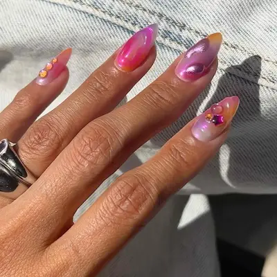 Hand with long almond nails with random 3D gel designs with a tie-dye base coat and chrome finish.