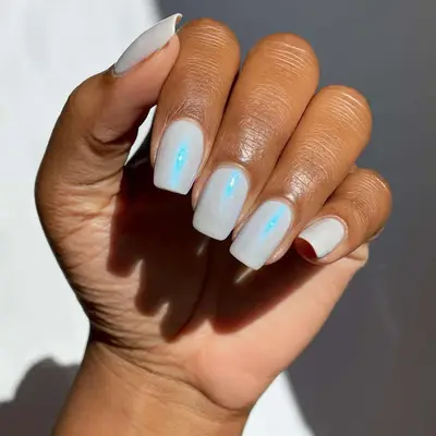 Hand with square nails, white base coat and a blue chrome finish