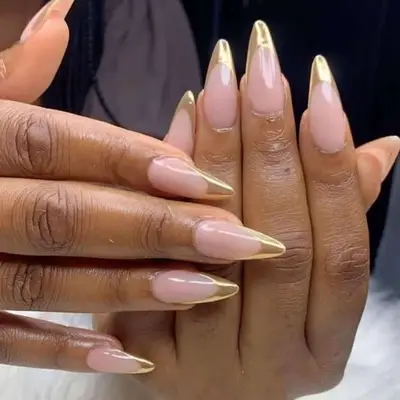 Hand with long stiletto nail shape with a gold french tip and light chrome top coat. 