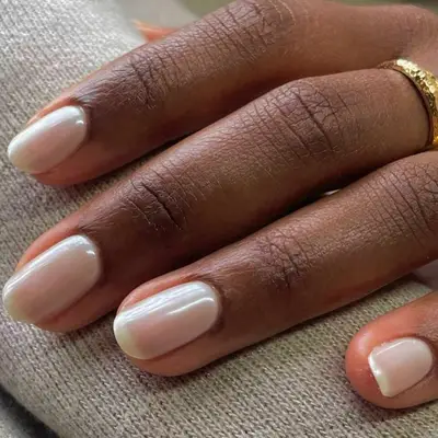Hand with short nails with a natural polish and light chrome finish. 