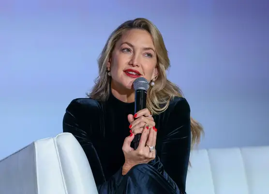 Kate Hudson holds a microphone in her fiery red nail polished hands.