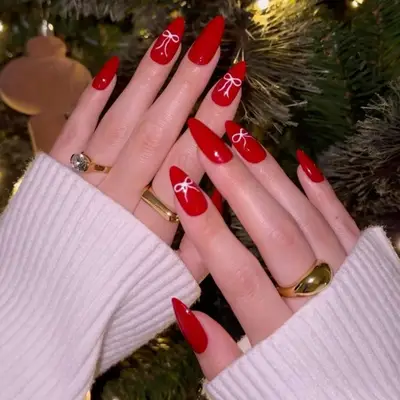 a red manicure with bow details, viewed against a Christmas tree