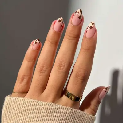 Cow-print manicure on short, stiletto-shaped nails.