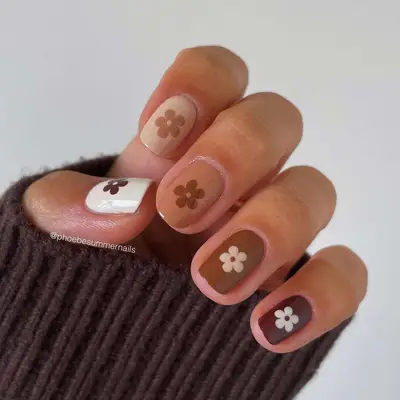 A manicure in various shades of brown, with daisies (also in shades of brown) on each finger