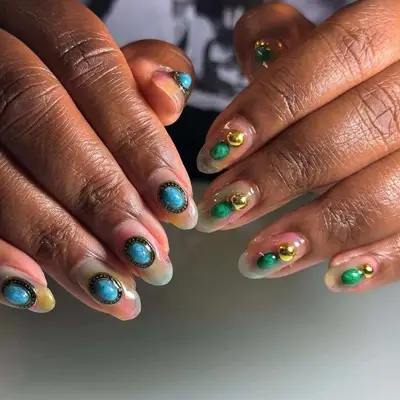 Close-up of hands with decorative nail art featuring turquoise stones and metallic accents