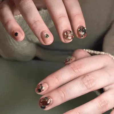 Close-up of hands with decorated long nails including cherries, lettering, and metallic accents