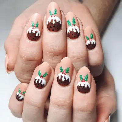 Nude oval nails with brown figgy pudding nail art topped with holly leaves.