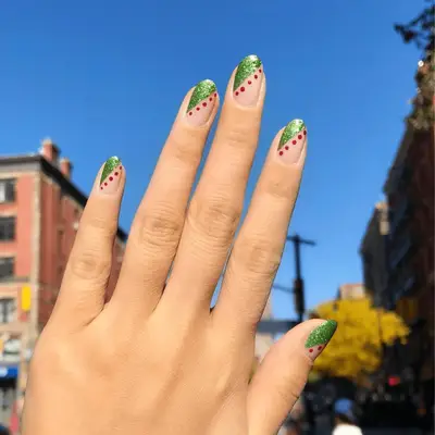 Short nails with a green glitter asymmetrical half French tip and red dot border.