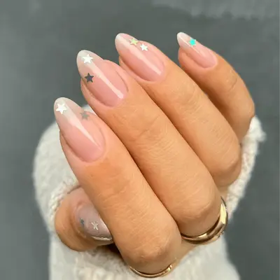 A close up of nude nails with silver sequin stars.