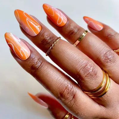 Hand with long nails featuring an abstract peachy ombre design, adorned with gold rings on fingers