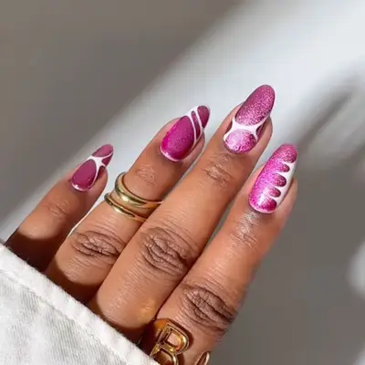 A hand with decorated nails featuring a magenta glass and velvet design, adorned with rings