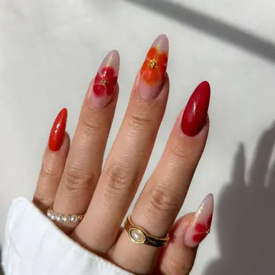 Hand with detailed floral and red nail art wearing gold and pearl rings