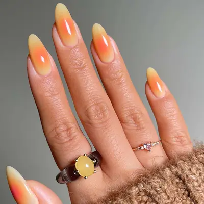 Manicure featuring long nails with a gradient yellow design resembling a sunburst, hand adorned with two rings