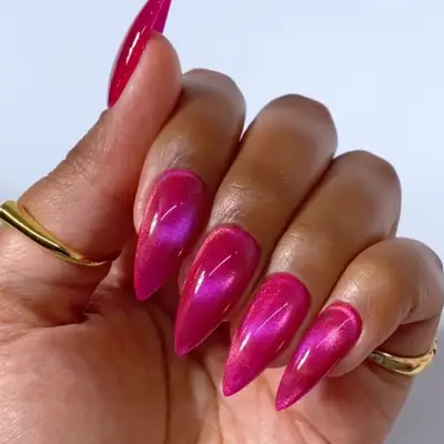 Hand with long almond-shaped fingernails with a sleek reflective finish, wearing minimal gold rings