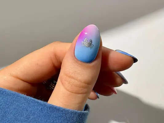 A hand displaying a nail with a crab symbol design on a gradient background