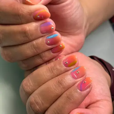 Hands showcasing nails with a colorful and glossy design, featuring gem accents