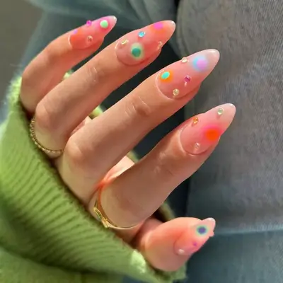 Close-up of a hand showcasing nail art with gemstones and colorful orb designs on almond-shaped nails