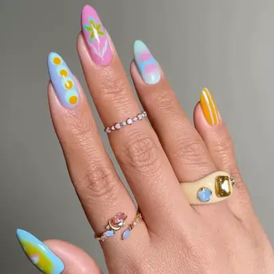 Hand with pastel-colored nail art featuring various patterns and designs, adorned with rings