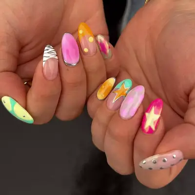 Manicure with colorful, mixed-design nails including stars, dots, and abstract patterns
