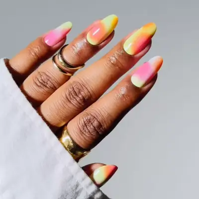 A hand with tie-dye inspired gradient nails in vibrant colors, adorned with gold rings