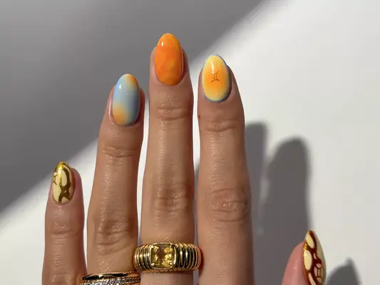 a hand with blue, orange, yellow, and gold nails in various designs